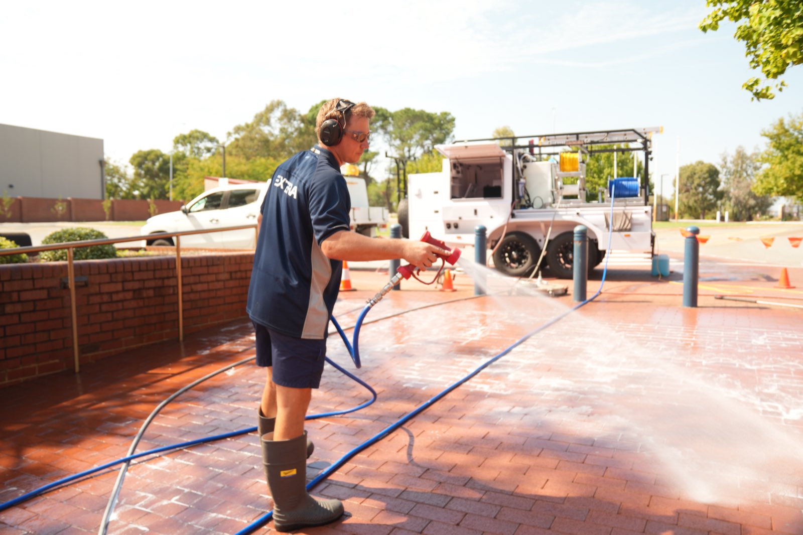 Extera operator washing a school forecourt with the truck-mounted rig behind